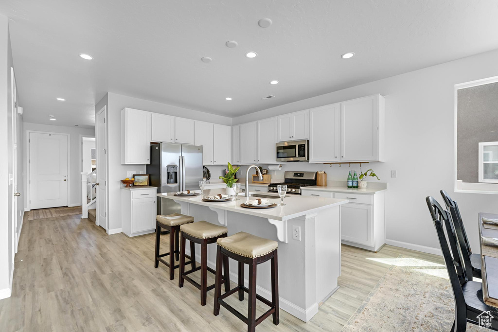 Kitchen featuring a breakfast bar, light wood-style floors, light countertops, stainless steel appliances, and baseboards