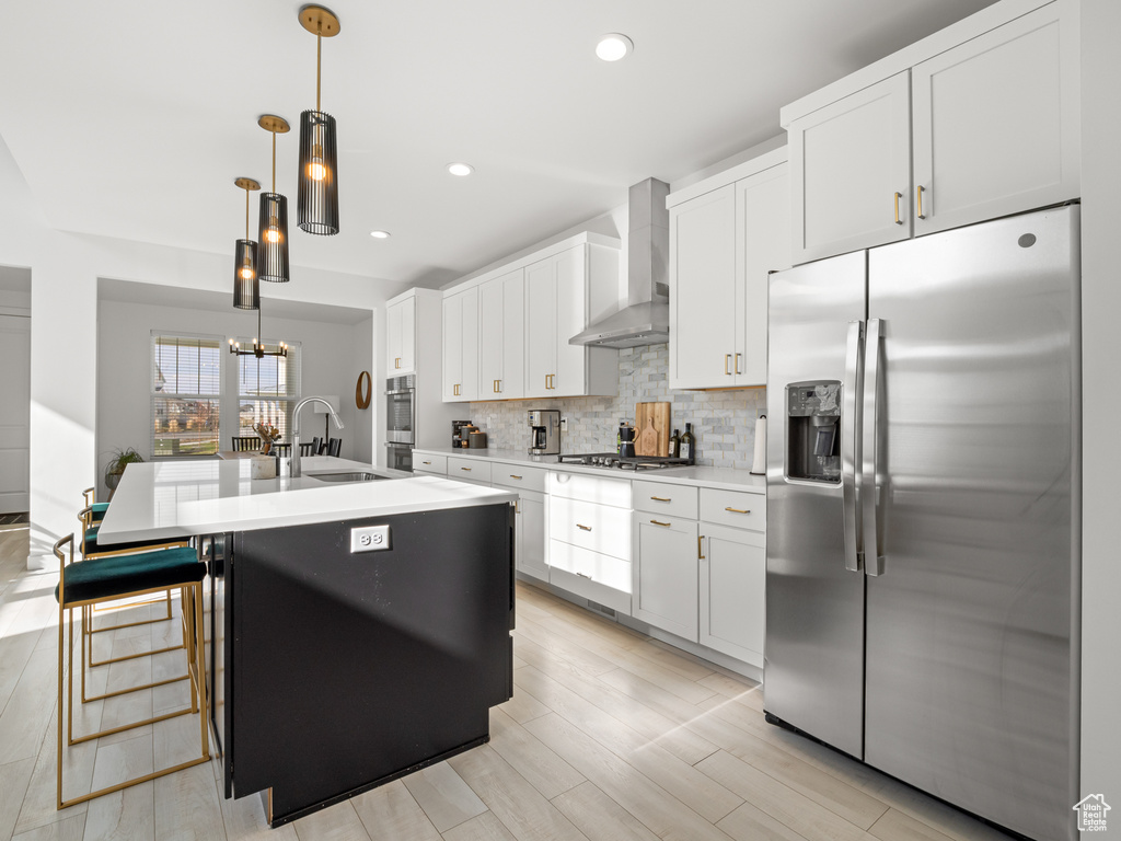 Kitchen featuring tasteful backsplash, wall chimney exhaust hood, a sink, appliances with stainless steel finishes, and a center island with sink