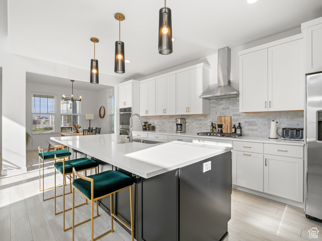 Kitchen featuring white cabinetry, backsplash, wall chimney exhaust hood, appliances with stainless steel finishes, and a sink