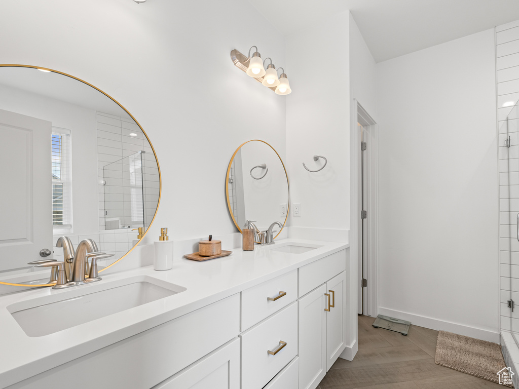 Full bath with a shower, double vanity, a sink, and wood finished floors