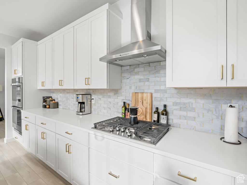 Kitchen with white cabinets, tasteful backsplash, wall chimney exhaust hood, and light countertops