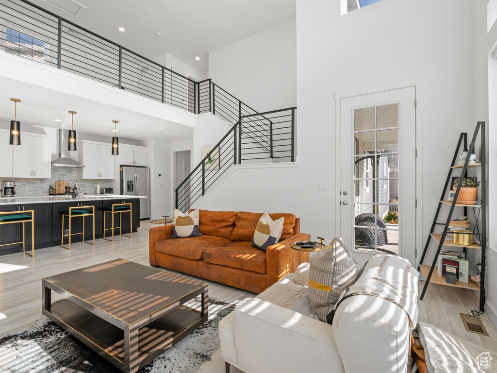 Living room with recessed lighting, light wood-type flooring, a towering ceiling, and stairs