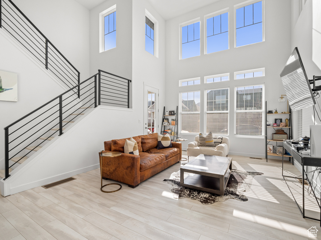 Living room with wood finished floors, a towering ceiling, visible vents, and stairway