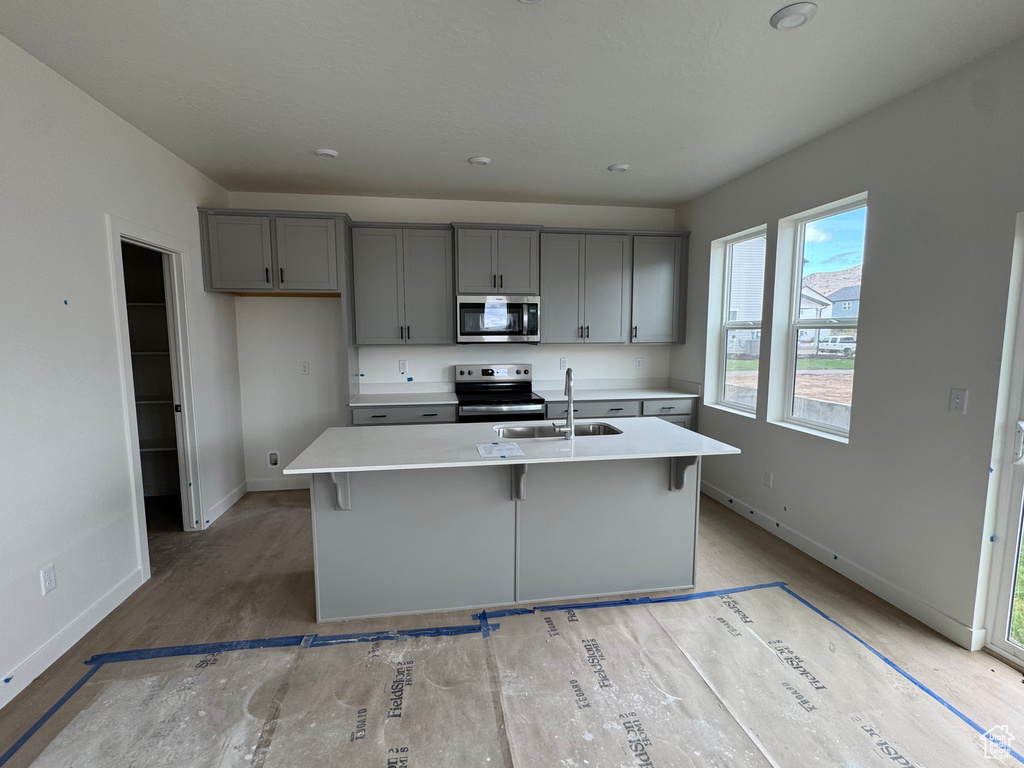 Kitchen with a sink, gray cabinets, baseboards, light countertops, and appliances with stainless steel finishes