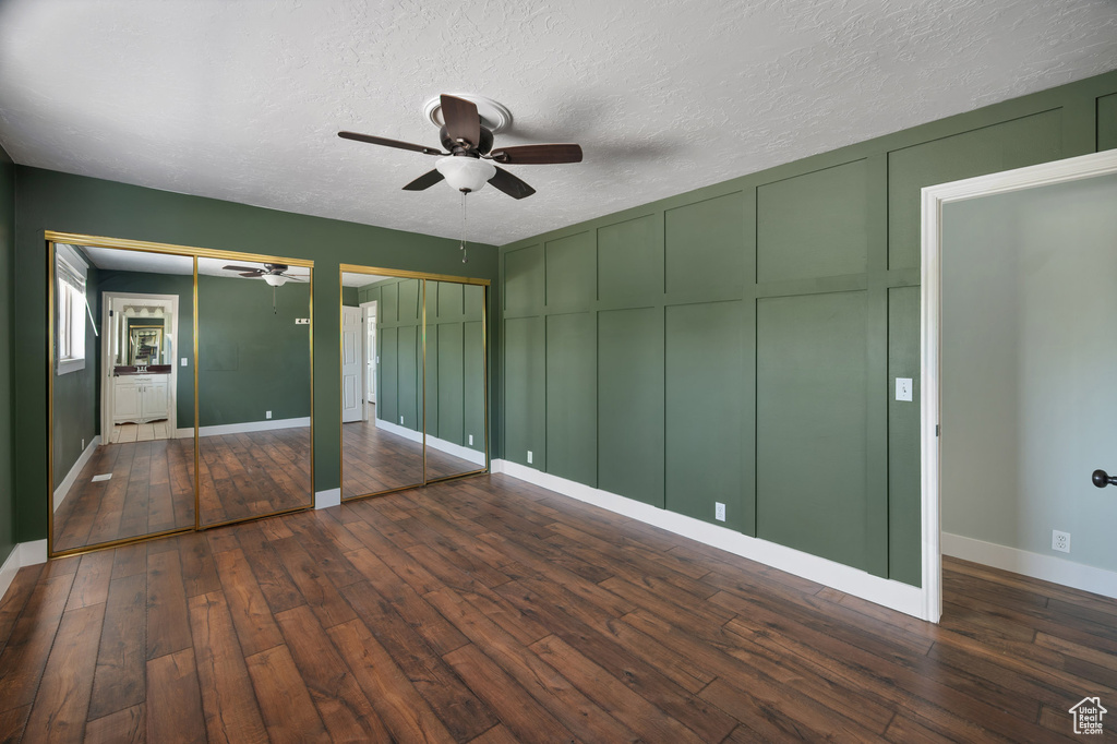 Unfurnished bedroom with wood-type flooring, baseboards, multiple closets, and a decorative wall