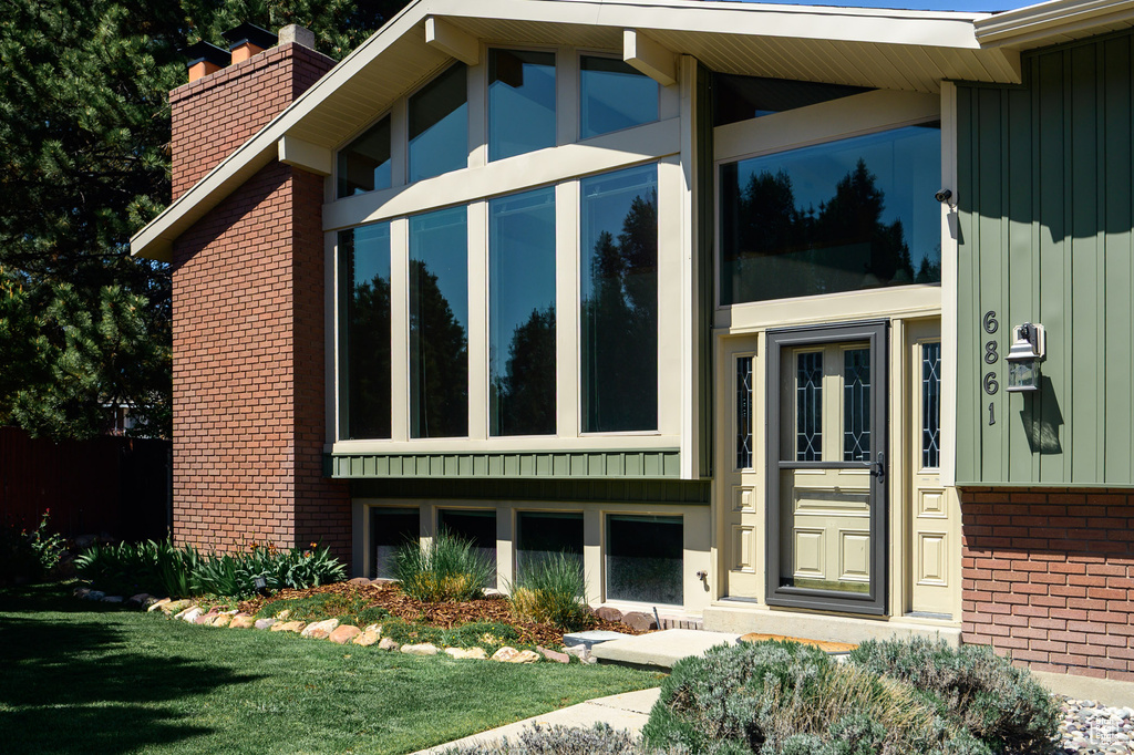 View of exterior entry featuring board and batten siding, brick siding, a yard, and a chimney