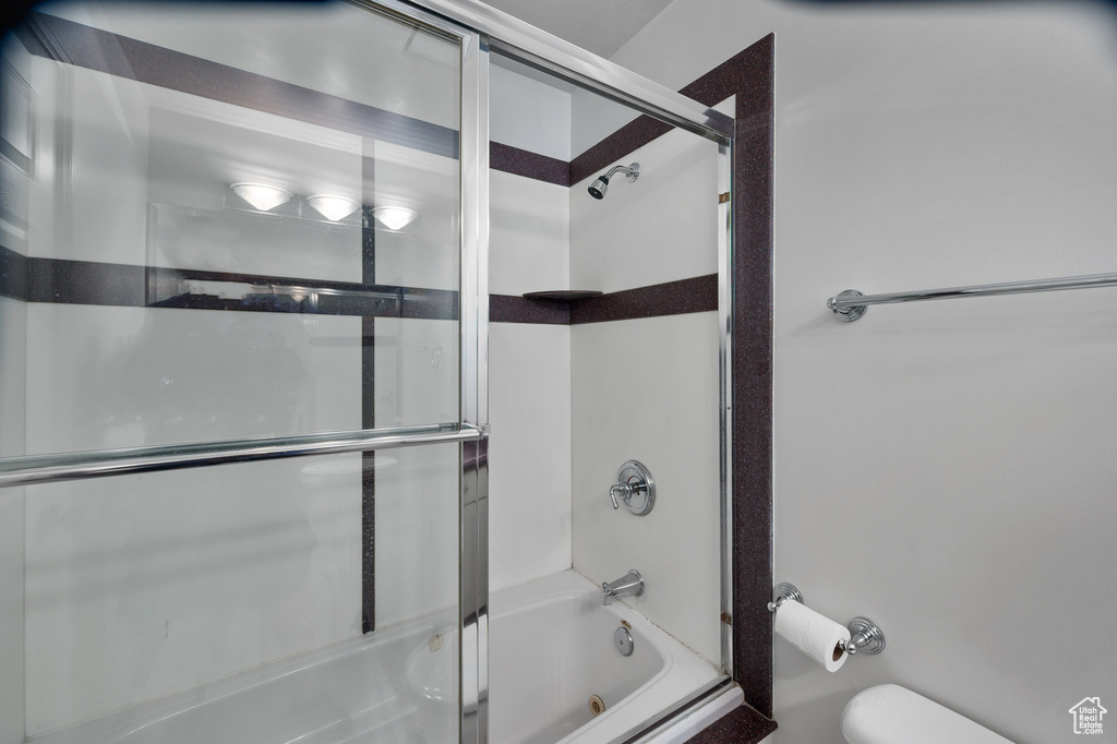 Bathroom with toilet and combined bath / shower with glass door