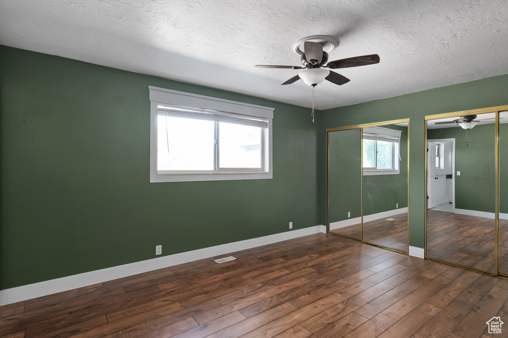 Unfurnished bedroom with multiple closets, baseboards, ceiling fan, dark wood-style floors, and a textured ceiling