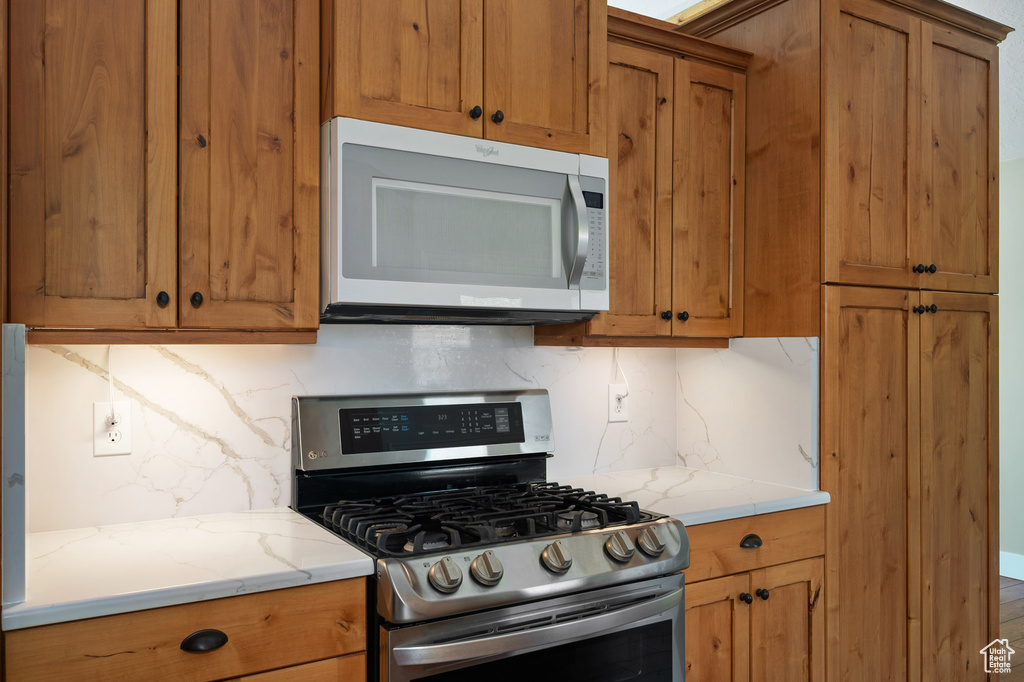 Kitchen with light stone counters, stainless steel gas range, brown cabinetry, and backsplash