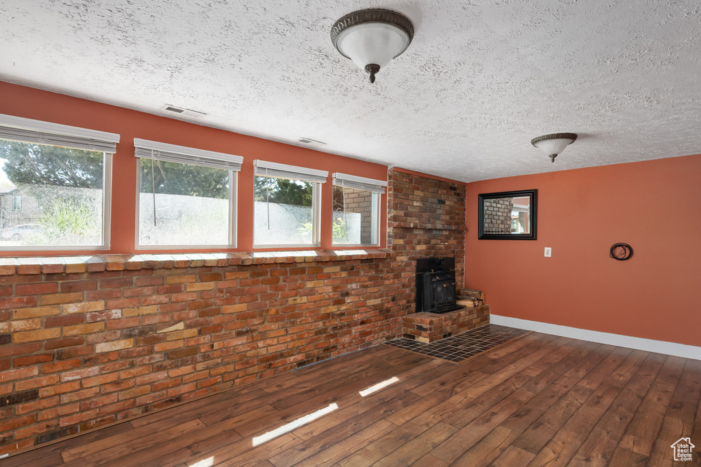 Unfurnished living room with brick wall, a textured ceiling, a wood stove, hardwood / wood-style flooring, and baseboards