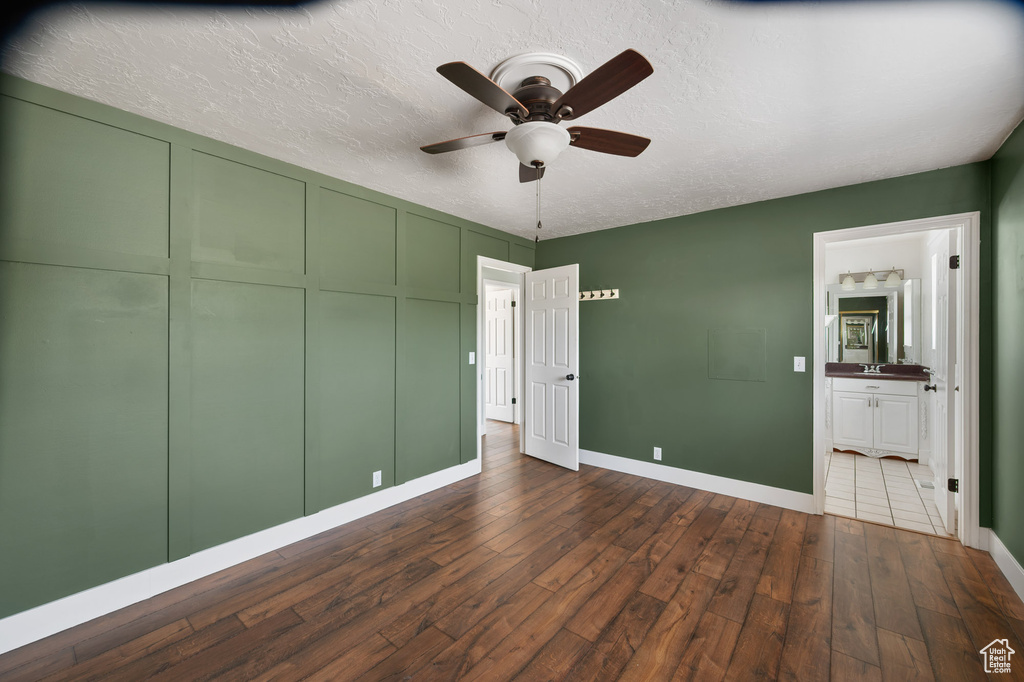 Unfurnished bedroom featuring dark wood-style flooring, baseboards, ensuite bathroom, a textured ceiling, and a ceiling fan