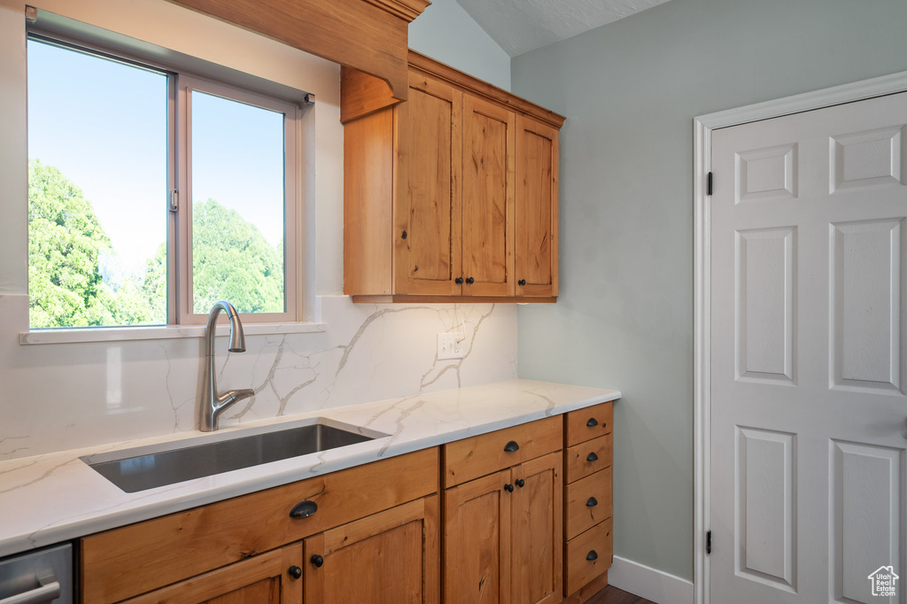Kitchen featuring brown cabinetry, decorative backsplash, a sink, and a healthy amount of sunlight