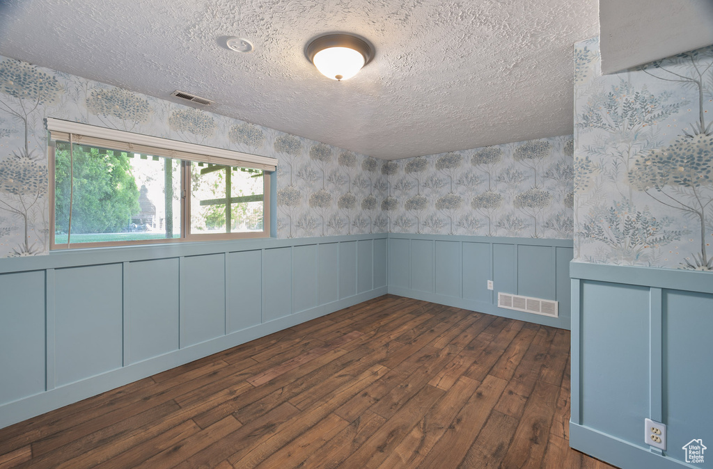 Empty room with visible vents, wainscoting, dark wood-style floors, and wallpapered walls