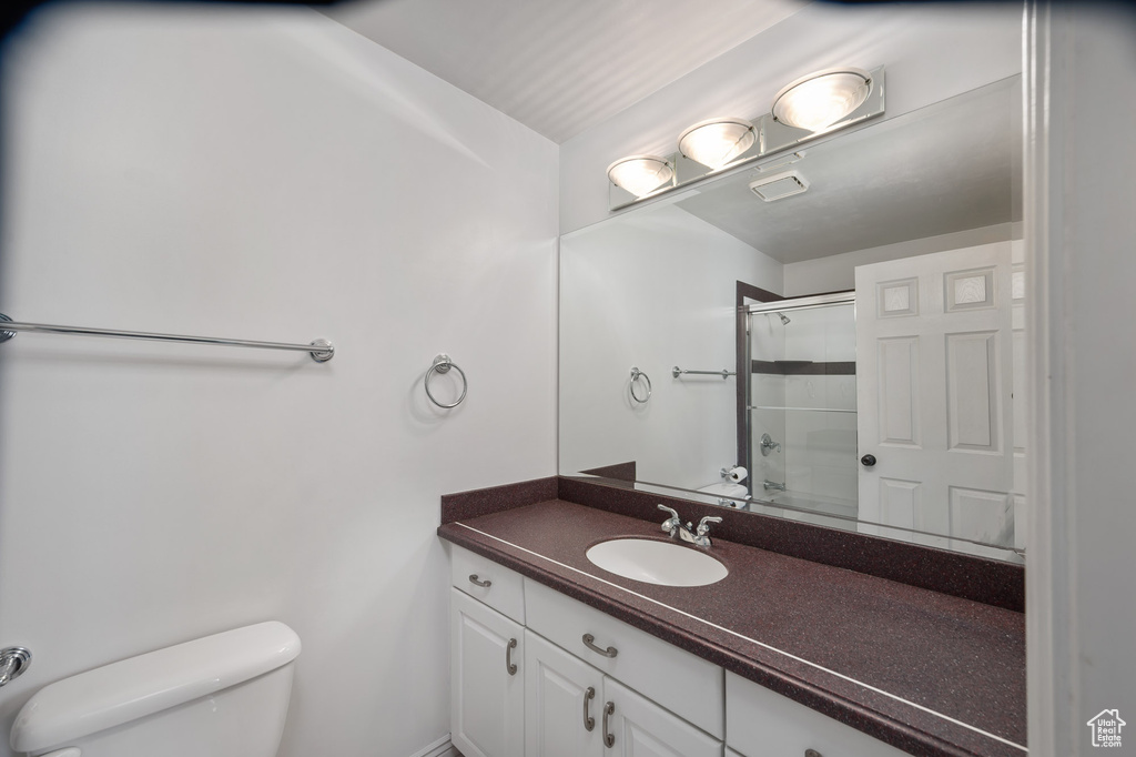 Bathroom with toilet, a shower with shower door, and vanity