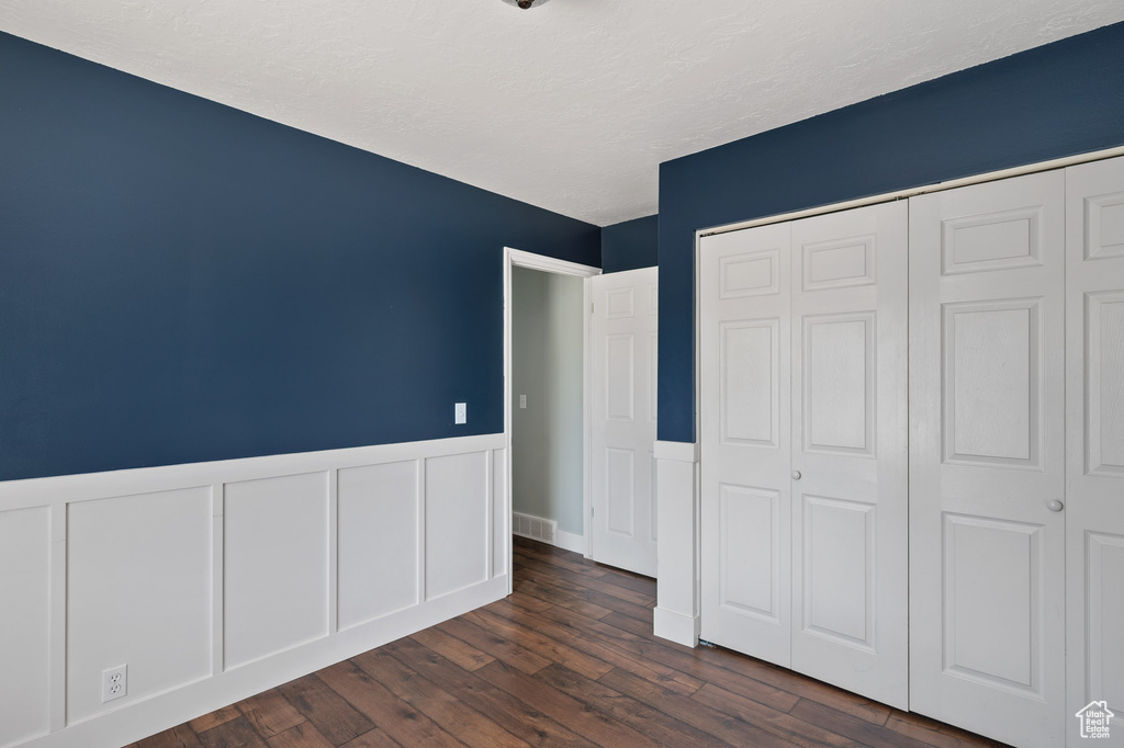 Unfurnished bedroom featuring wainscoting, a textured ceiling, dark wood finished floors, visible vents, and a closet
