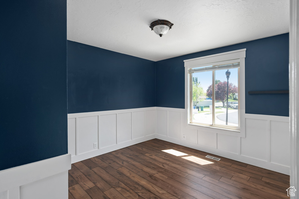 Unfurnished room with visible vents, wainscoting, and dark wood-style floors