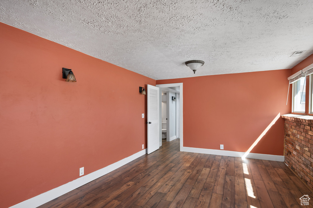 Spare room with baseboards, hardwood / wood-style flooring, a textured ceiling, and visible vents