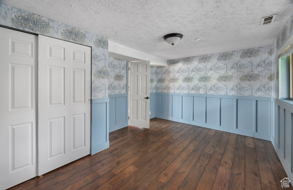 Spare room with a textured ceiling, wainscoting, hardwood / wood-style floors, and wallpapered walls