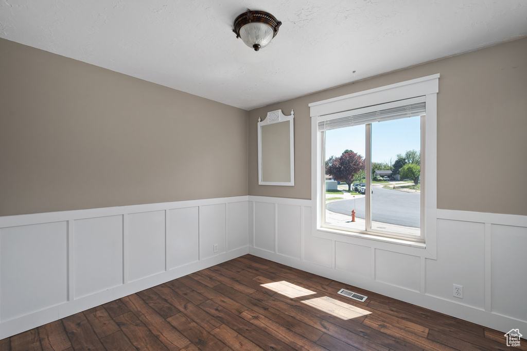 Empty room featuring wainscoting, visible vents, dark wood-style floors, and a decorative wall