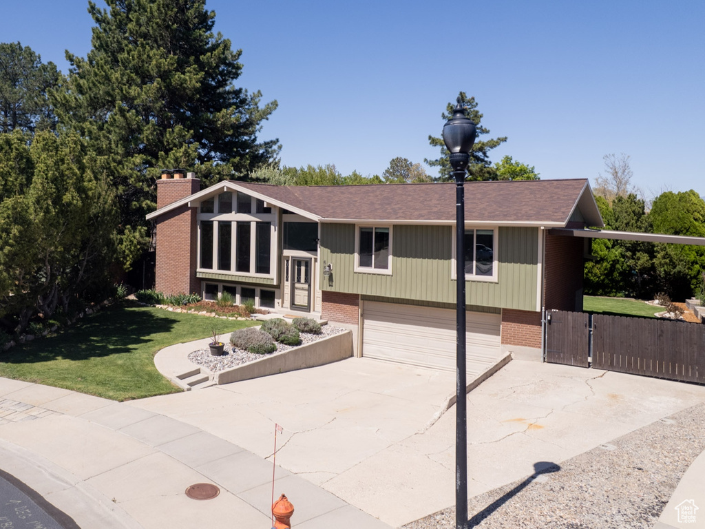 View of front of home with a front yard, a chimney, brick siding, an attached garage, and driveway