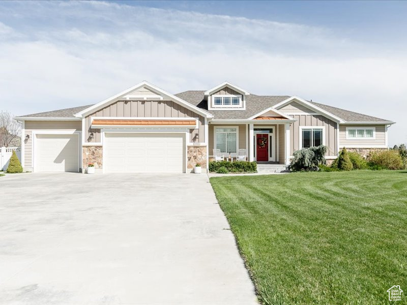 Craftsman-style home with board and batten siding, driveway, a front yard, an attached garage, and stone siding