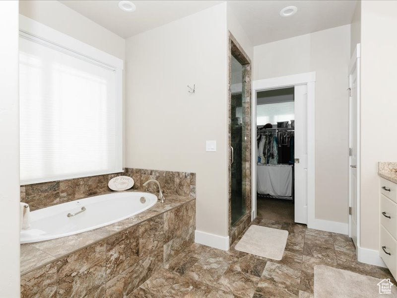 Bathroom with a bath, a stall shower, vanity, baseboards, and a spacious closet