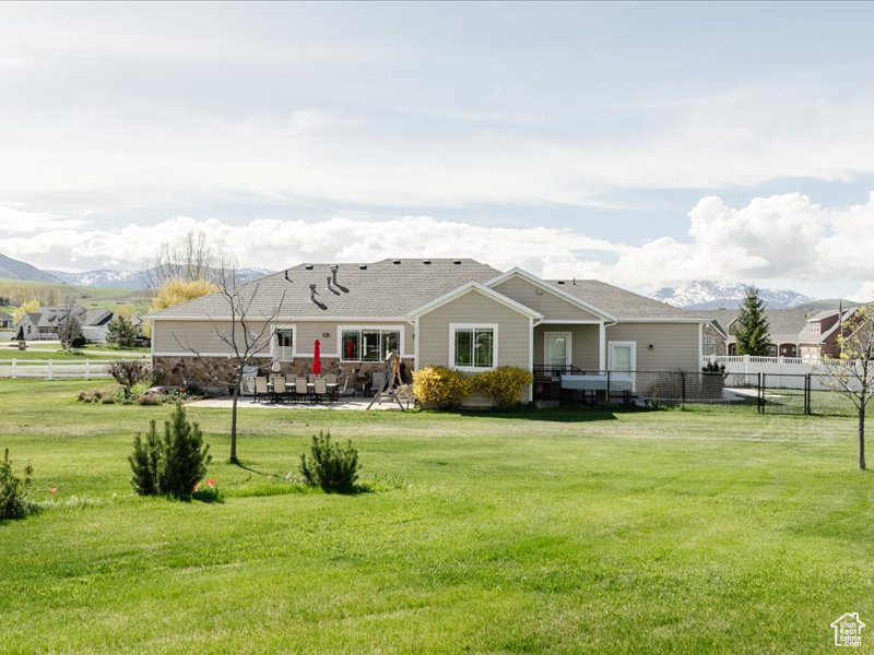 Back of house featuring a lawn, a mountain view, fence, and a patio