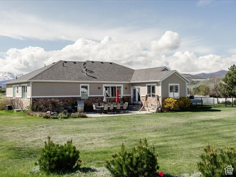 Rear view of house with fence, a yard, a patio area, and stone siding