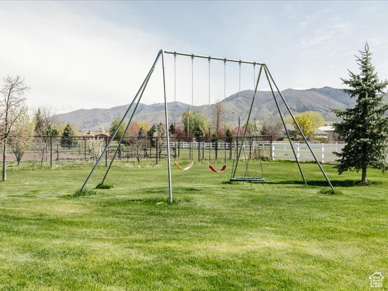 View of playground with a lawn, a rural view, fence, and a mountain view