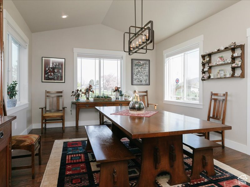 Dining area featuring baseboards, a notable chandelier, dark wood finished floors, and lofted ceiling