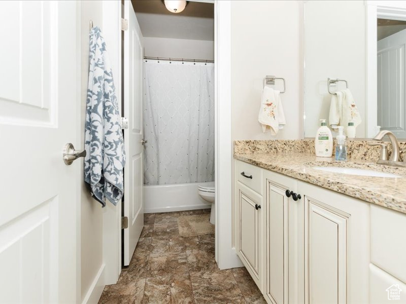 Bathroom featuring toilet, stone finish flooring, shower / bath combination with curtain, and vanity