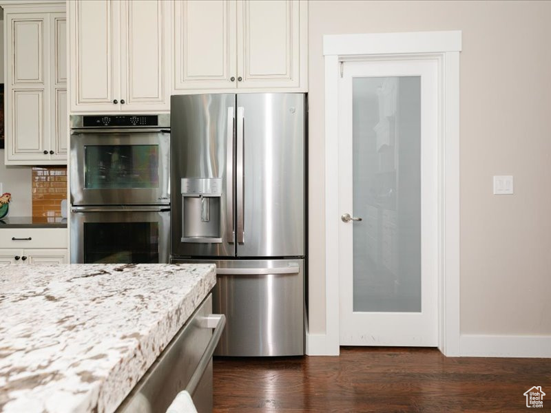 Kitchen featuring baseboards, dark wood finished floors, light stone countertops, and stainless steel appliances