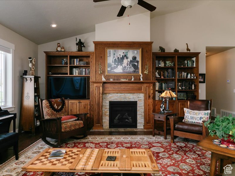 Sitting room featuring wood finished floors, a ceiling fan, lofted ceiling, and a stone fireplace