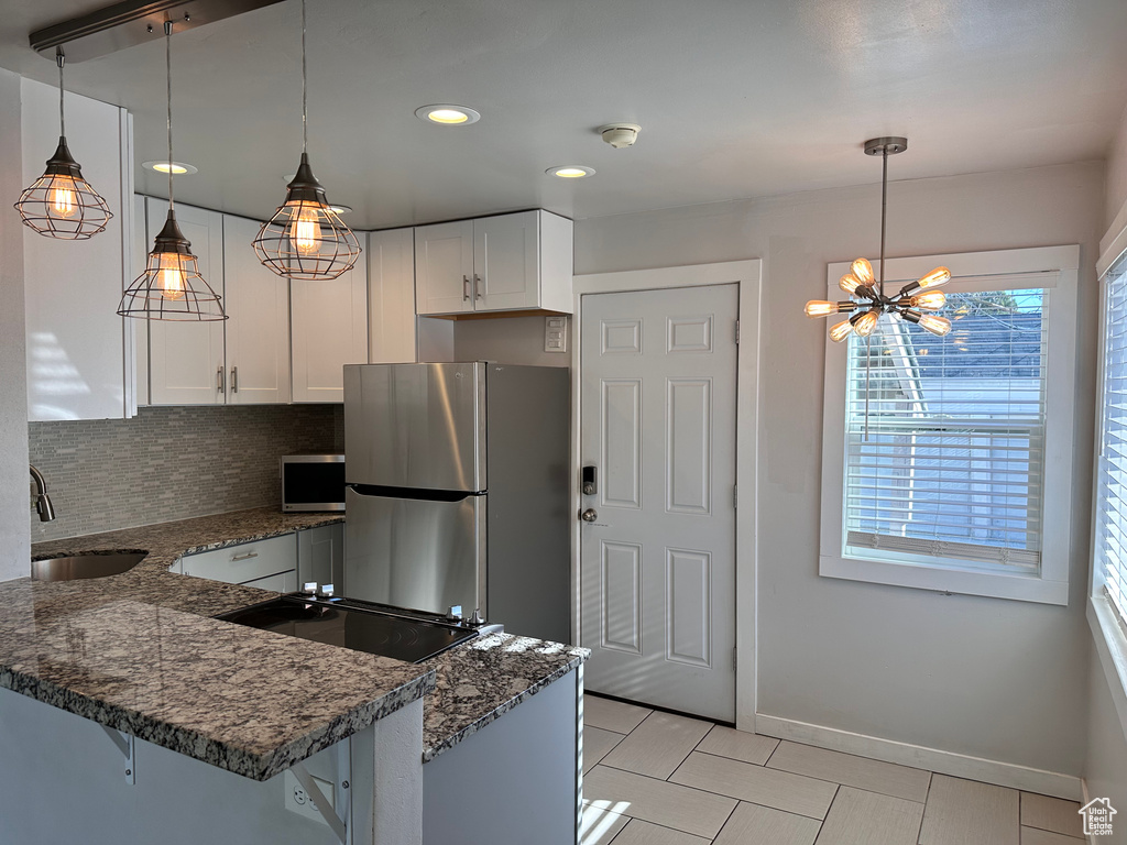 Kitchen with white cabinets, a sink, dark stone countertops, stainless steel appliances, and light tile patterned floors