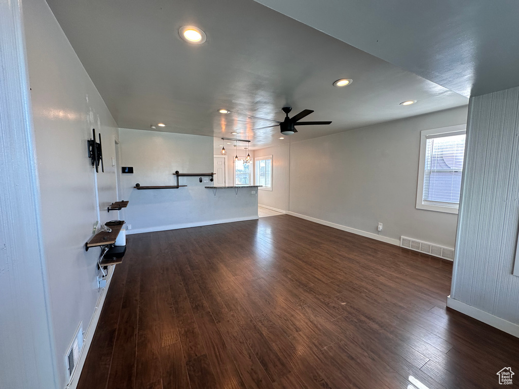 Unfurnished living room with a ceiling fan, baseboards, visible vents, and dark wood-type flooring