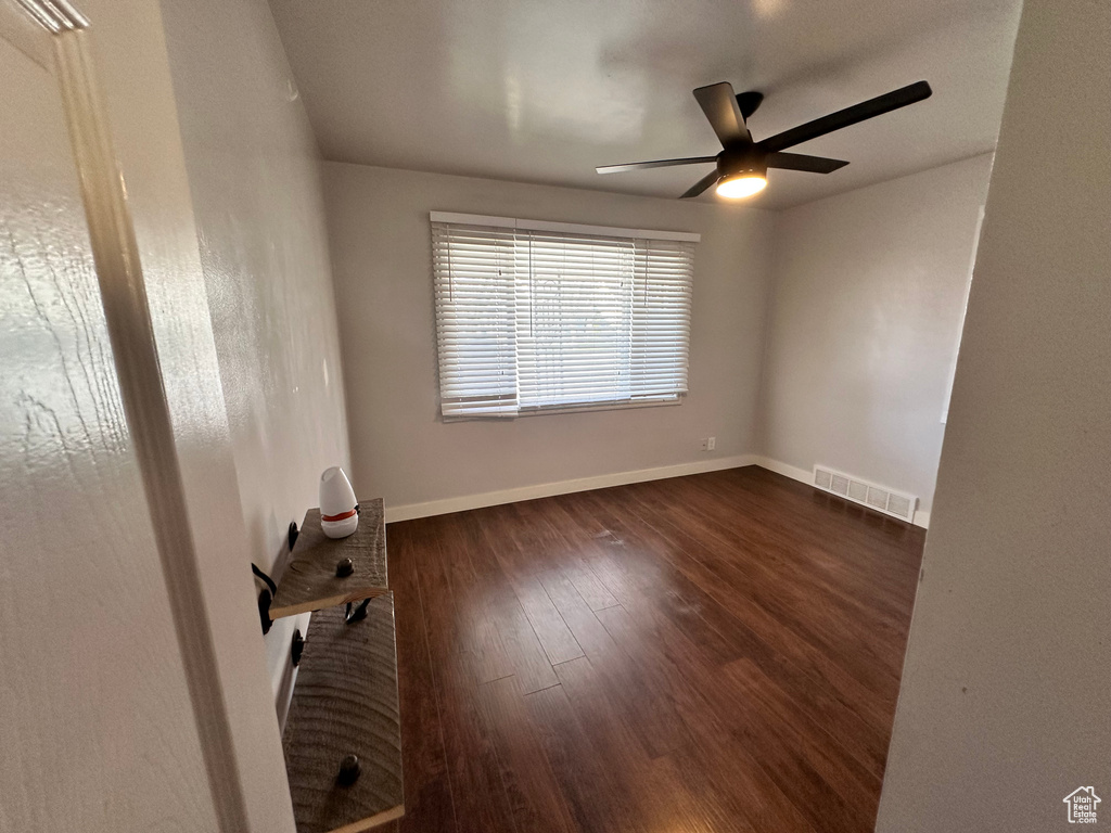 Empty room featuring visible vents, a ceiling fan, baseboards, and dark wood-type flooring