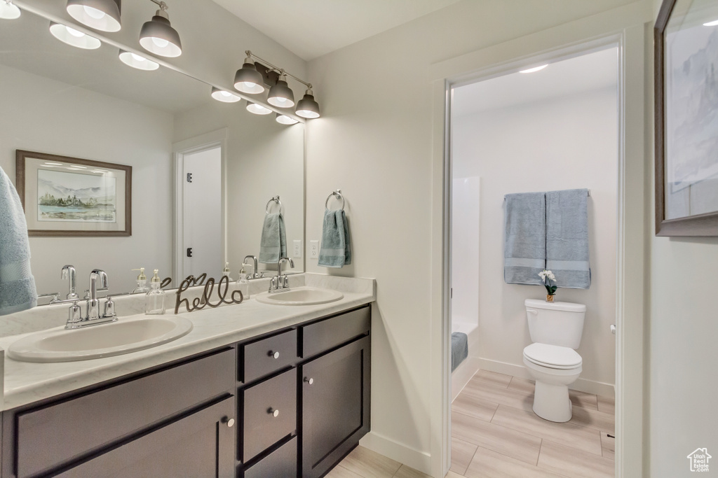 Bathroom with toilet, a sink, double vanity, and baseboards