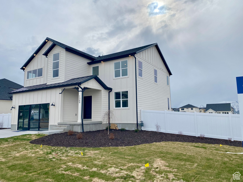 Modern farmhouse with a front lawn, a standing seam roof, fence, and board and batten siding