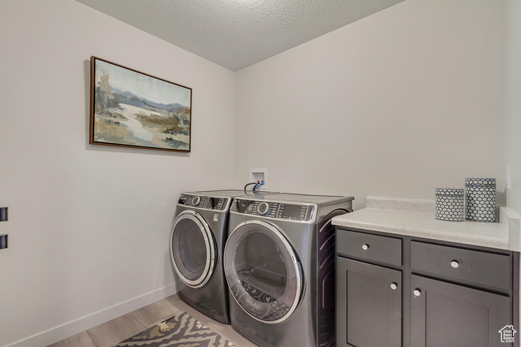 Washroom featuring baseboards, a textured ceiling, washing machine and clothes dryer, light wood finished floors, and cabinet space