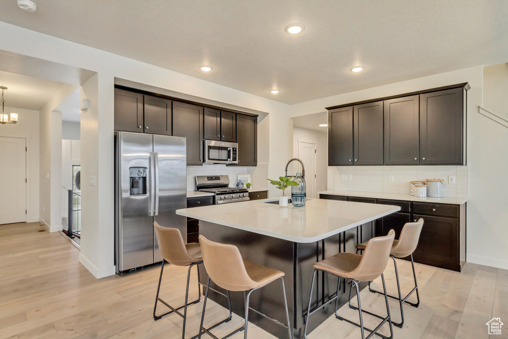 Kitchen featuring a sink, a breakfast bar area, appliances with stainless steel finishes, a center island with sink, and light wood-style floors