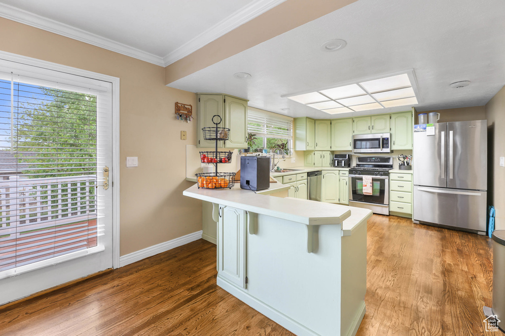 Kitchen with crown molding, light countertops, stainless steel appliances, a peninsula, and green cabinets