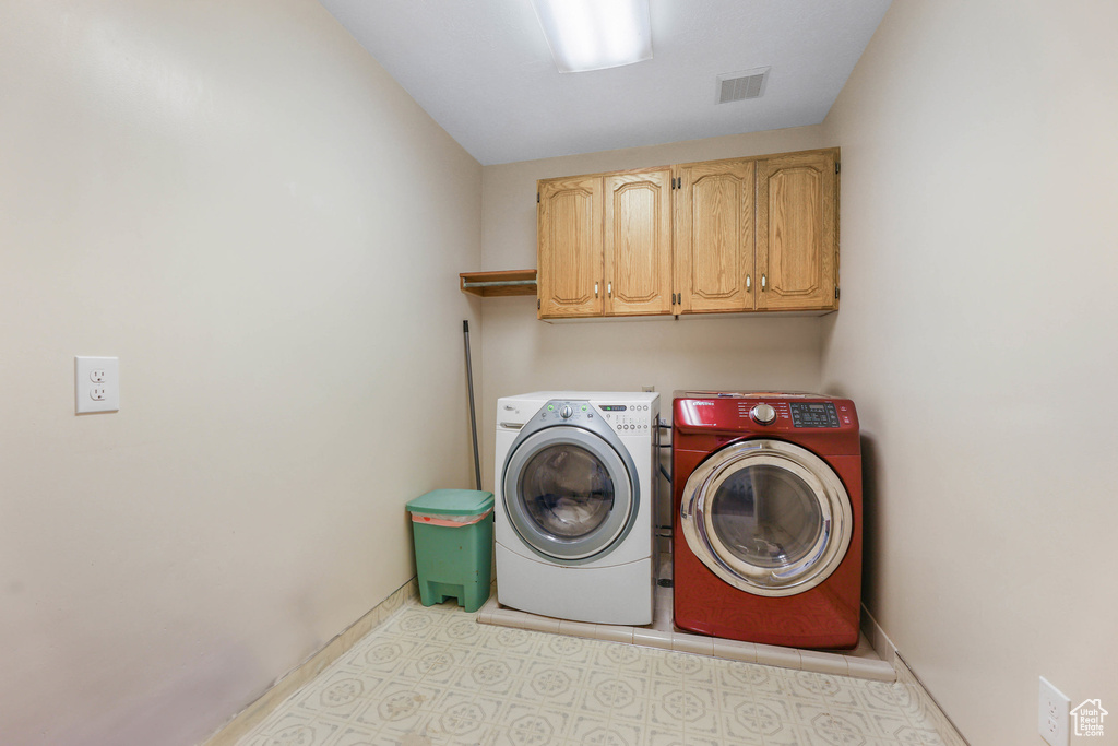Washroom with cabinet space, baseboards, light floors, visible vents, and washing machine and dryer
