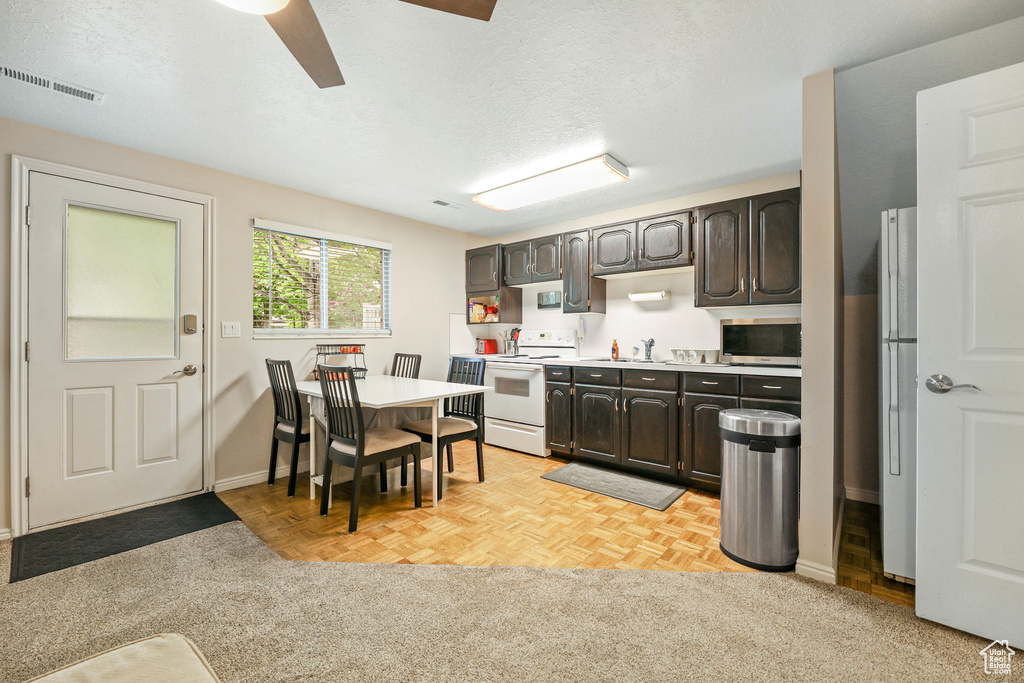 Kitchen featuring dark brown cabinetry, visible vents, a sink, light countertops, and white appliances