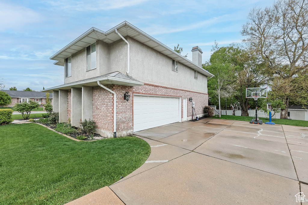 View of side of property with brick siding, stucco siding, a chimney, concrete driveway, and a yard