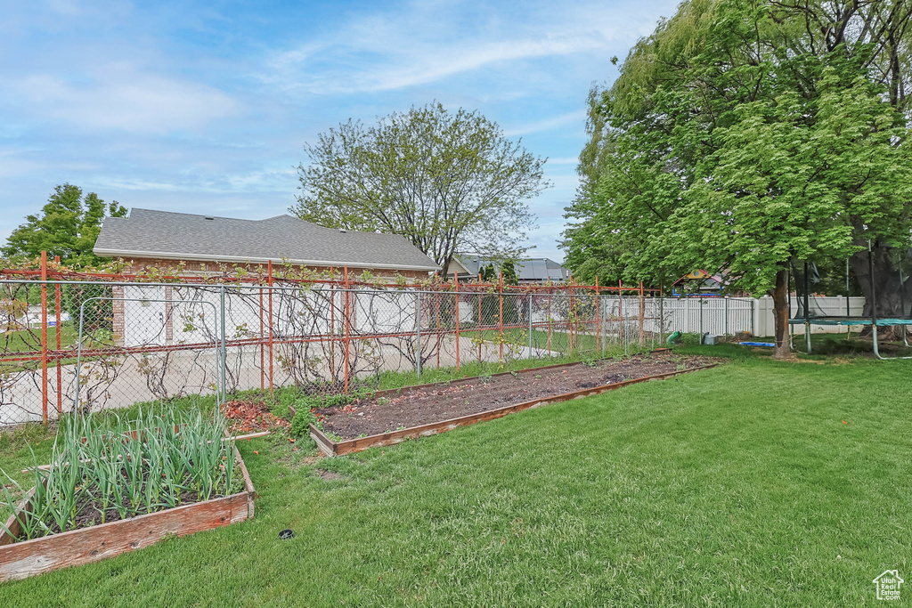 View of yard with a trampoline, fence, and a vegetable garden