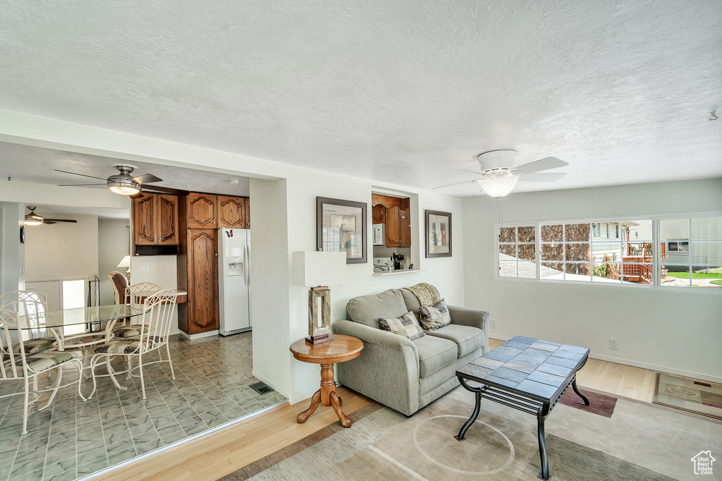 Living room with light wood-style floors, a textured ceiling, baseboards, and ceiling fan
