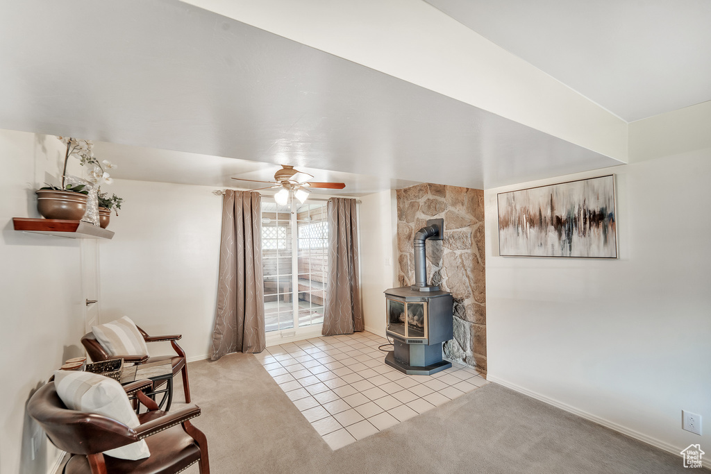 Carpeted living area with baseboards, a wood stove, a ceiling fan, and tile patterned floors