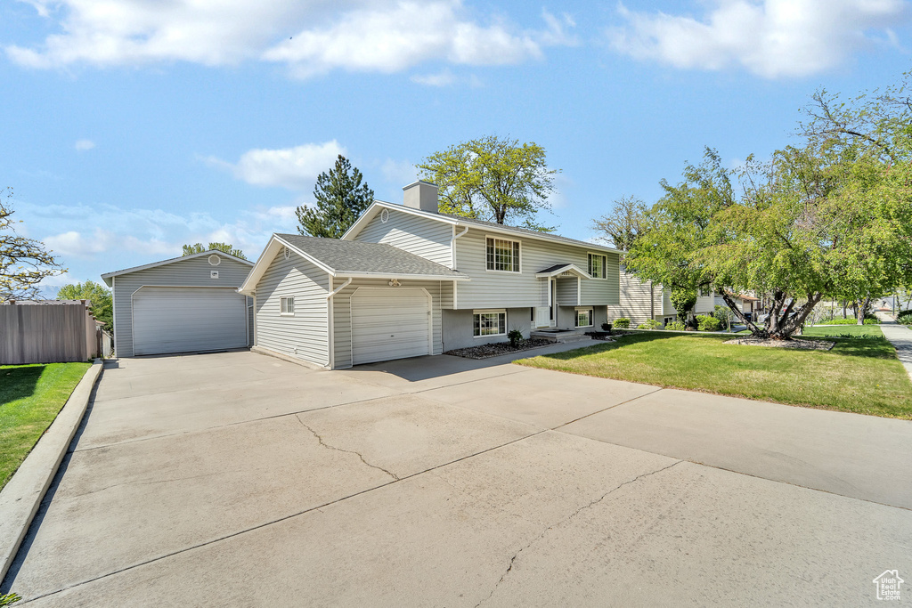 Bi-level home featuring fence, an attached garage, a shingled roof, a front lawn, and a chimney