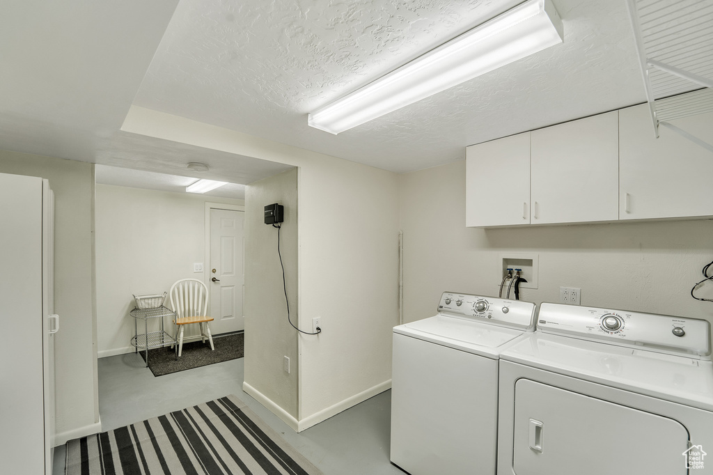 Laundry room featuring separate washer and dryer, baseboards, a textured ceiling, and cabinet space