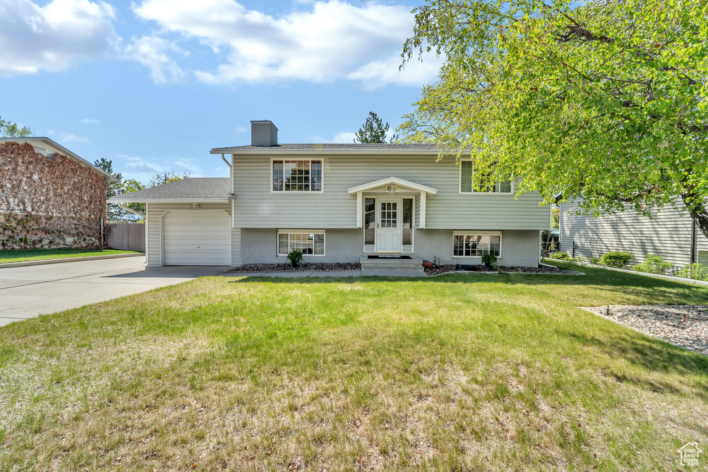 Split foyer home featuring fence, a garage, a front yard, a chimney, and driveway